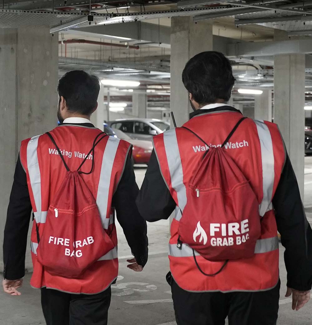 Two JustAsk waking watch officers carrying fire grab bags and walkie-talkies while patrolling an underground car park as part of a fire safety inspection